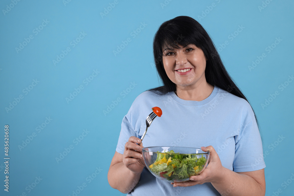 Beautiful overweight woman eating salad on light blue background, space for text. Healthy diet Beautiful overweight woman eating salad on light blue background, space for text. Healthy diet