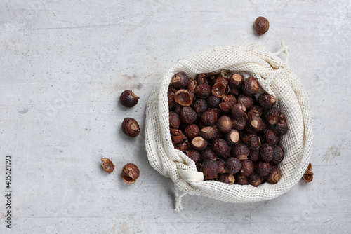 Soap nuts or soapberries (sapindus mukorossi)  natural detergent in a cotton bag on a gray concret table flat lay  with copy space. Sustainable  and vegan lifestyle. photo