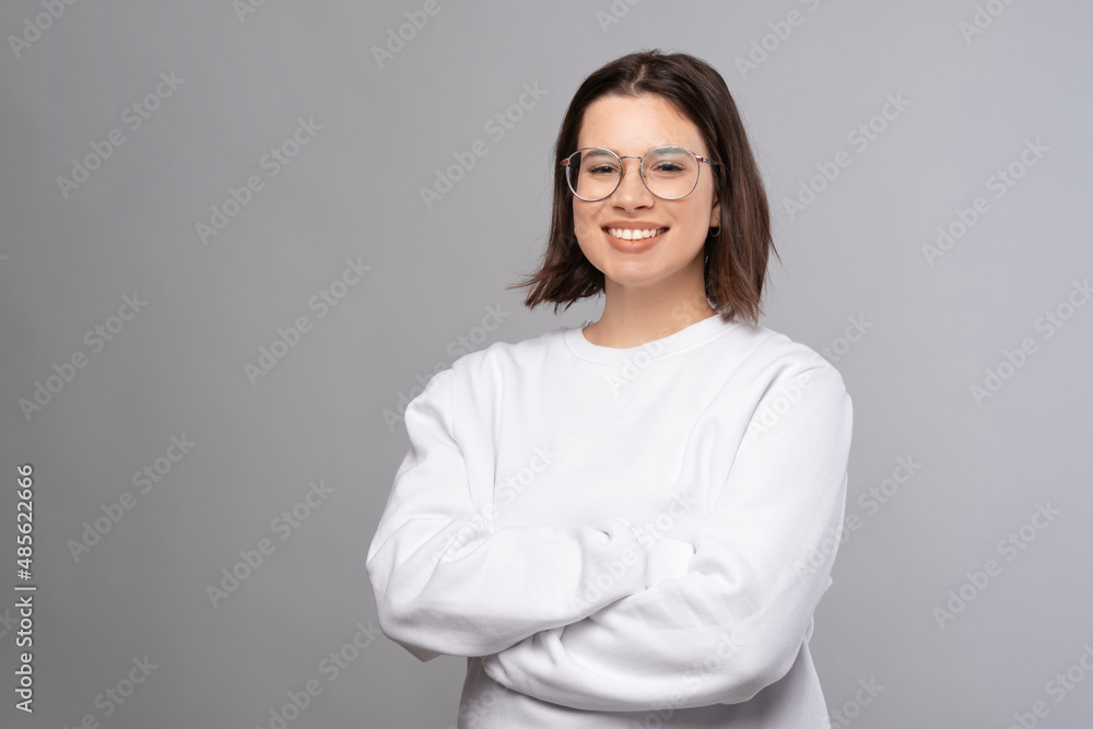 Young woman wearing glasses is standing with crossed arms smiling at the camera over grey background. Young woman wearing glasses is standing with crossed arms smiling at the camera over grey background.