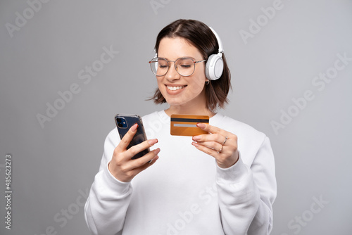 Young lady is paying music subscription over phone with credit card. Portrait over grey background. photo