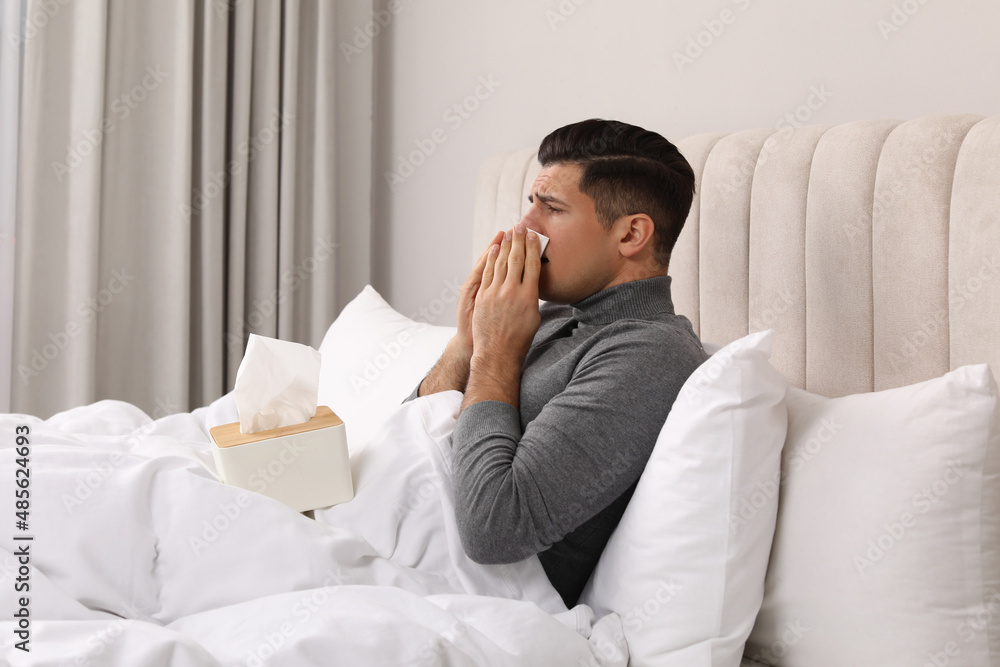 Sick man with box of paper tissues suffering from cold in bed at home