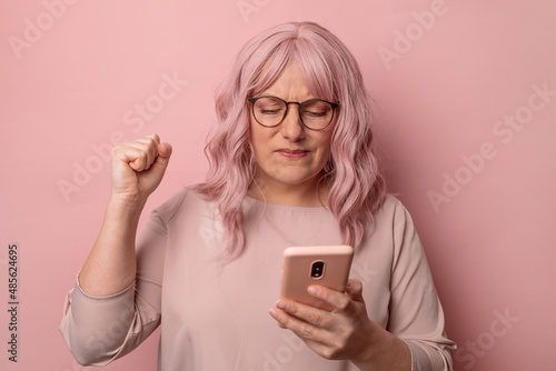 Stressed european millennial 30s woman in a stylish blouse using mobile phone with negative expression standing isolated on pink background.