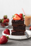 Pieces of fresh chocolate brownie with strawberries on a concrete background. Stack of fudgy chocolate brownies with strawberries on a concrete background. Homemade bakery and dessert.