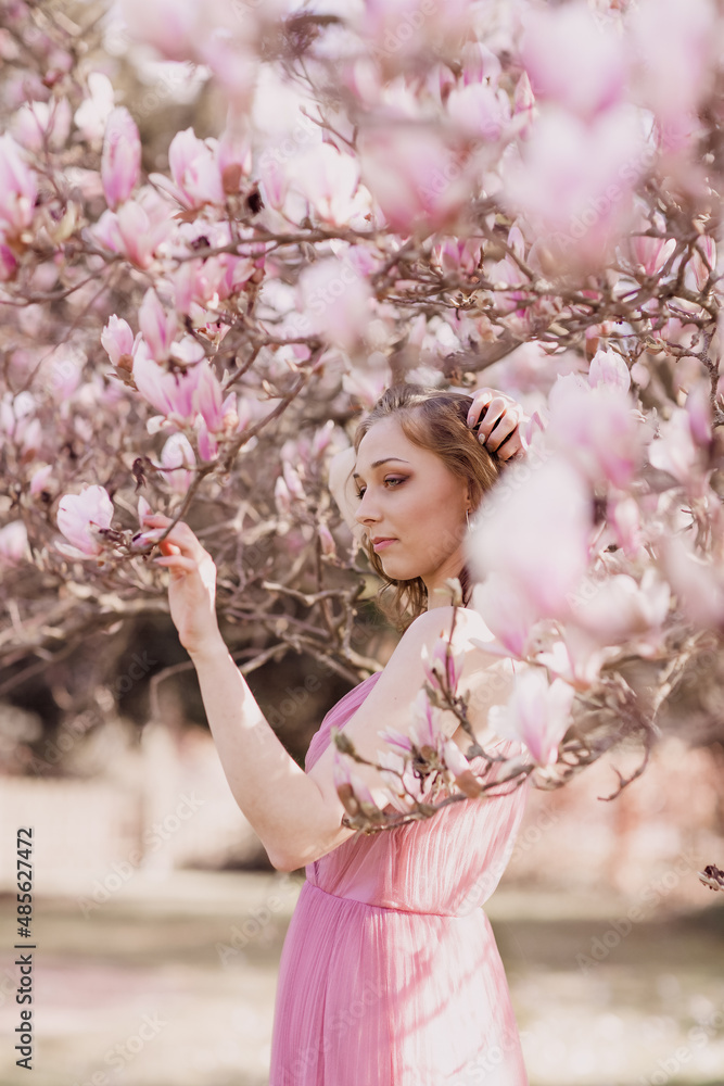 Spring flowering. Portrait of a young blonde girl in the branches of a blooming magnolia. Open aperture with light blurring and illumination. Spring flowering. Portrait of a young blonde girl in the branches of a blooming magnolia. Open aperture with light blurring and illumination.