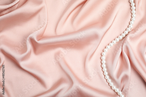 Beautiful pearls on pink silk, top view. Space for text photo