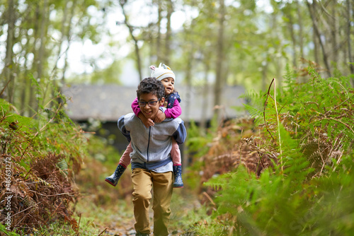 Brother piggybacking sister on trail in woods photo