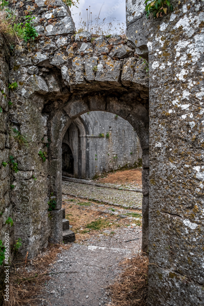 Ancient stone walls with arched passage in Rozafa Castle in Shkoder, Albania. Inner courtyard of a medieval ruined fortress, vertical
