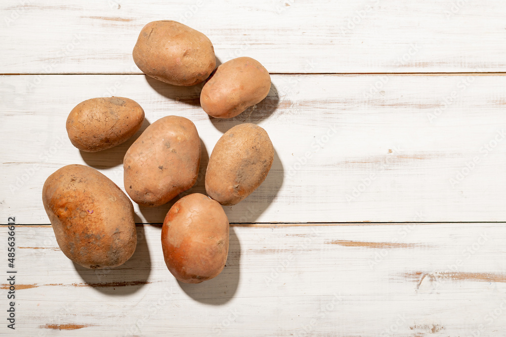 Raw potato tubers on a light wooden background. Unpeeled dirty potatoes. Raw potato tubers on a light wooden background. Unpeeled dirty potatoes.
