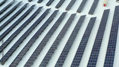 Close up new solar farm standing in rows of modern photovoltaic panels in at winter with snow falling. Drone shoots video of energy saving and concept of alternative power source 