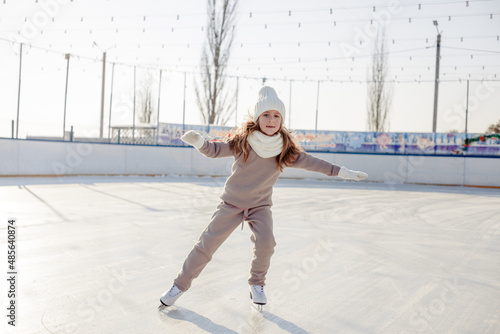 Funny little blonde girl of 7 years old in casual clothes posing on a skating rink in skates. The concept of a child's lifestyle. Layout of the copy space.