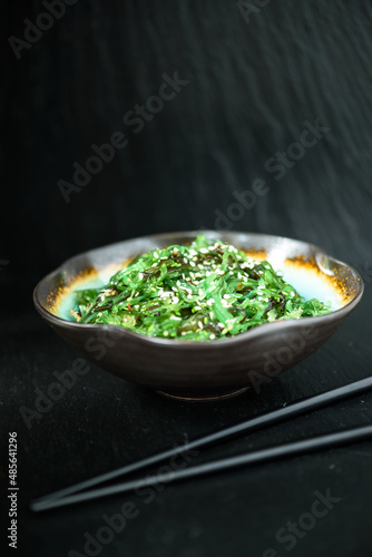 Wakame - Sea Algae Salad beautifully presented in a handmade porcelain bowl, with chopsticks on a dark background