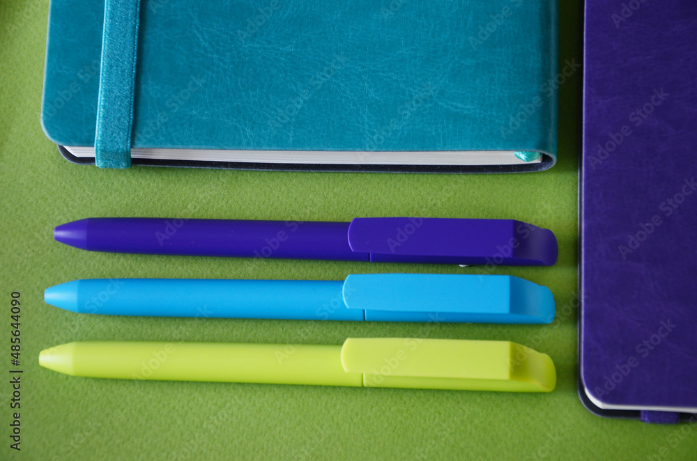 Bright notepads and colored pens on a background of colored paper. writing accessories. Corporate gifts for office employees. Sunny mood for work. Bright notepads and colored pens on a background of colored paper. writing accessories. Corporate gifts for office employees. Sunny mood for work.