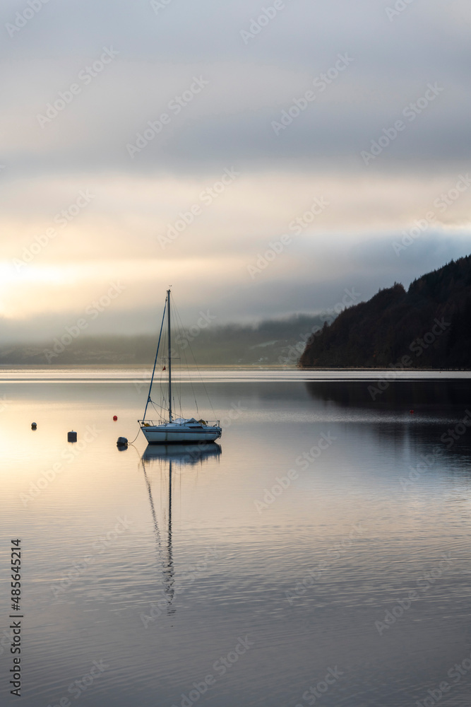 Sailing boat under dramatic sunset sky on Loch Tay Lake at sunset, Kenmore, Perthshire, Highlands of Scotland, United Kingdom, Europe