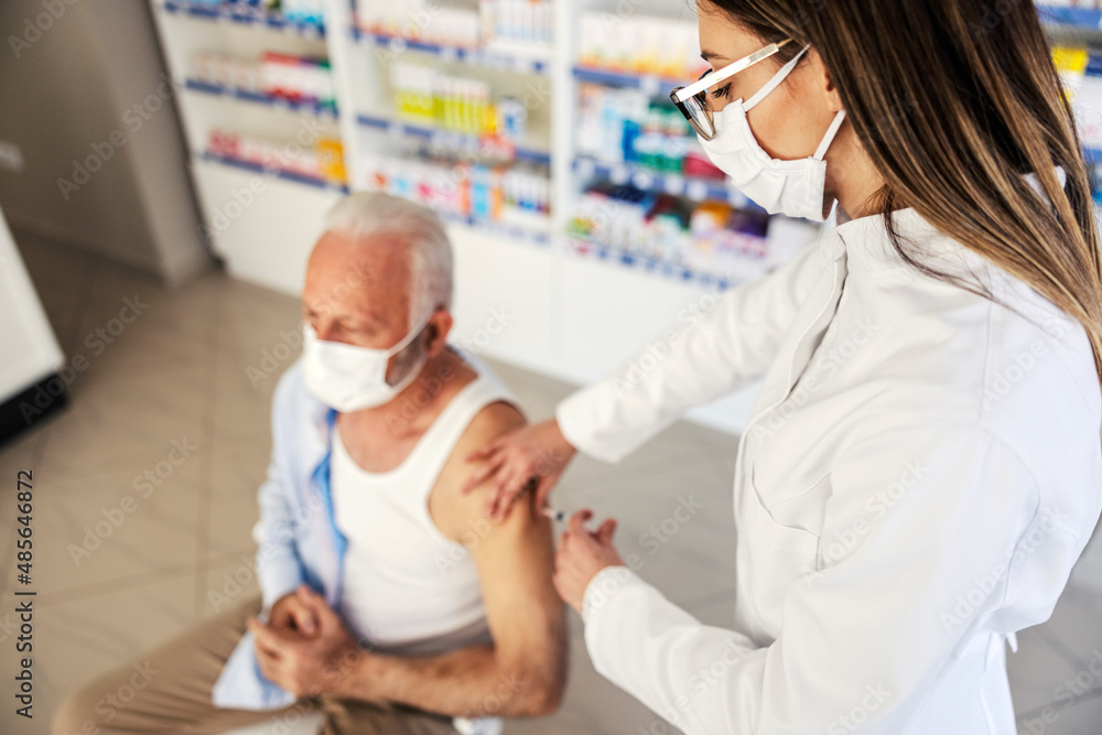 A nurse injecting cure into an old man's shoulder at pharmacy. A nurse injecting cure into an old man's shoulder at pharmacy.