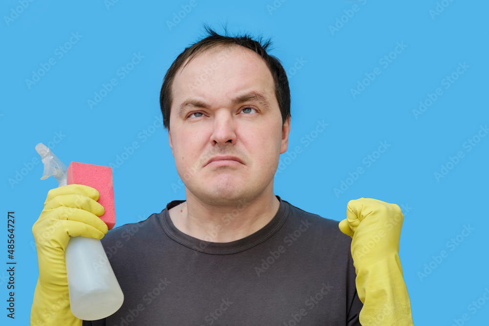 Angry male cleaner in yellow gloves, studio blue background Angry male cleaner in yellow gloves, studio blue background