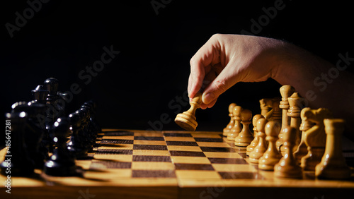 A man hand with a chess piece in a board game. Opening of the chess game with the move of the white king pawn e2-e4, copy space on a black background
