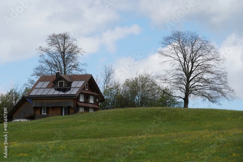 Wooden house with solar panels on the roof. Lonely wooden house in Swiss countryside equipped with modern technology for production of electricity from renewable sources. Copy space available. 
