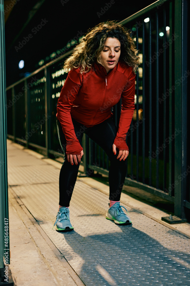 A young fit sportswoman taking a break and resting after a long run at the train station at night. A night runner taking a break in the urban exterior. A young fit sportswoman taking a break and resting after a long run at the train station at night. A night runner taking a break in the urban exterior.