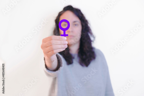 Portrait of a young woman holding a woman symbol close to her eye. Feminism concept.