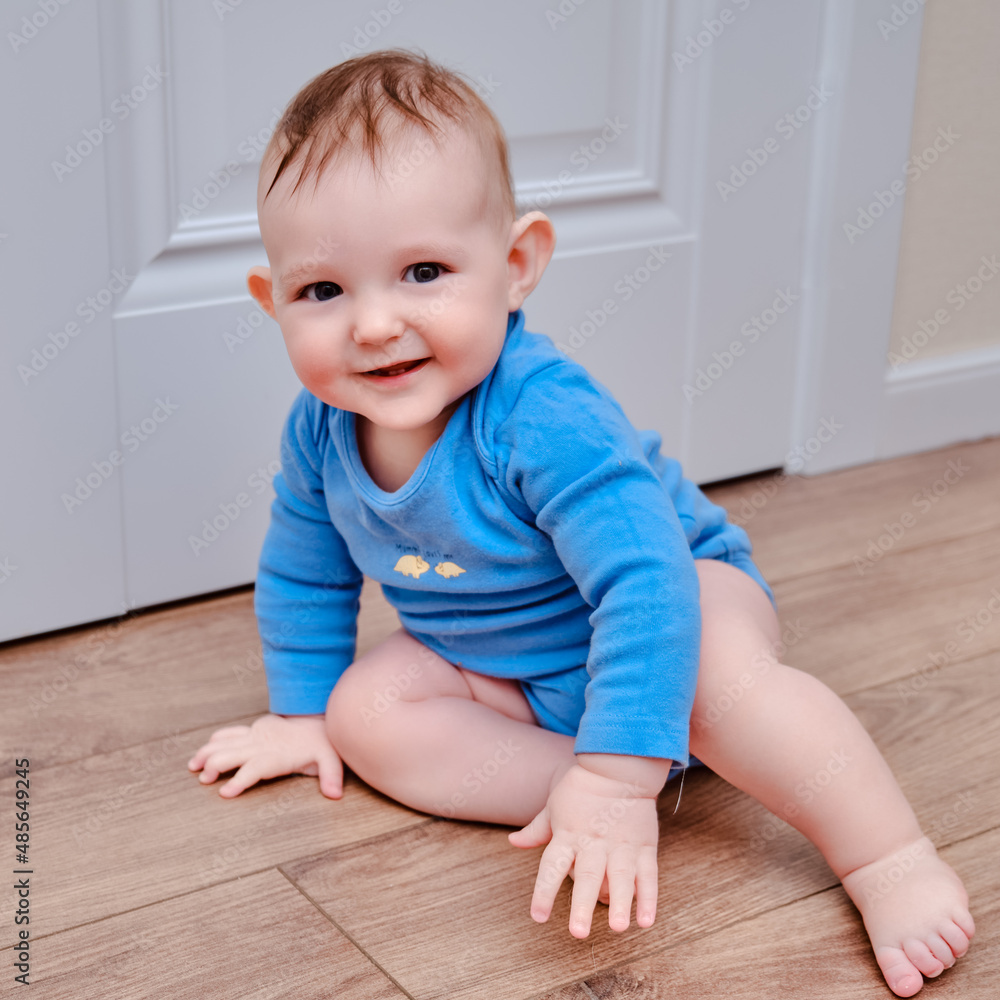 Happy baby toddler crawls on a wooden laminate. Funny child is sitting smiling on the parquet in the home living room, aged 6-11 months Happy baby toddler crawls on a wooden laminate. Funny child is sitting smiling on the parquet in the home living room, aged 6-11 months