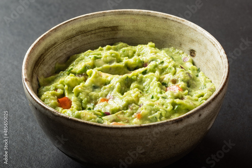 Traditional Mexican Guacamole sauce made from avocado. lime, red onion, tomatoes, cilantro on a pink background.
