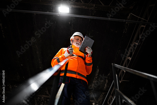 Professional heavy industry engineer worker wearing safety uniform and hard hat, using tablet computer controlling production.