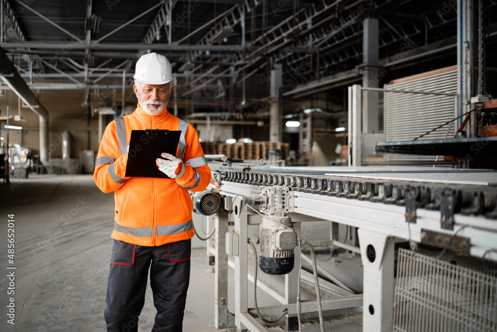 Industrial worker supervisor standing by machine and checking production in manufacturing factory.