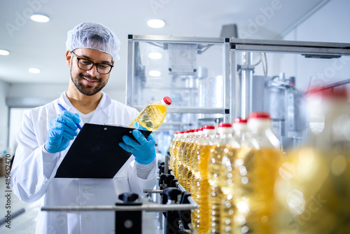 Food factory worker inspecting product quality and controlling production of refined edible bottled oil. photo