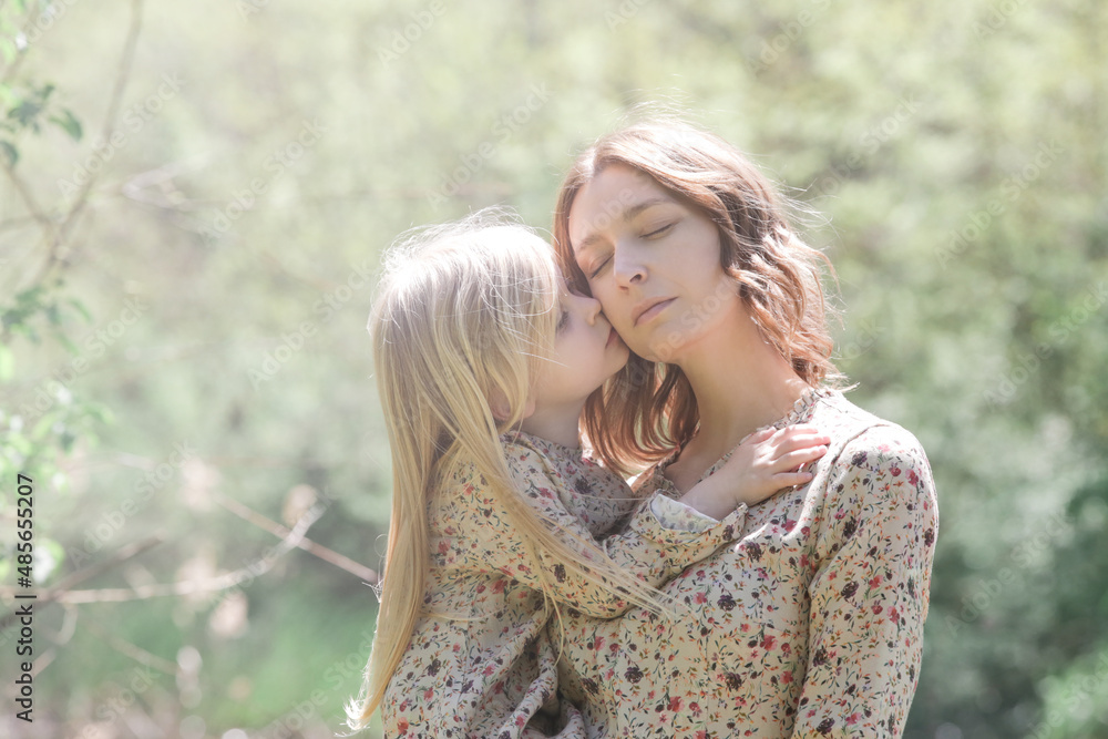 Mother and daughter in matching dress hugging during idyllic summer day. Carefree family time outdoor. Mother and child love. Mother and daughter in matching dress hugging during idyllic summer day. Carefree family time outdoor. Mother and child love.