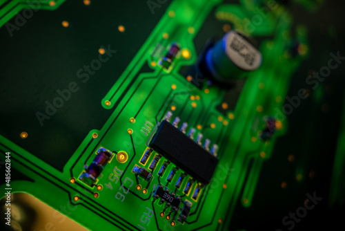Fototapeta Naklejka Na Ścianę i Meble -  Detail of a microprocessor, resistors and capacitors soldered to a green glowing PCB printed circuit board with various connections and contacts