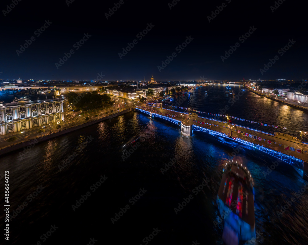 Fototapeta premium Night landscape of festivities on the day of the Russian Navy, picturesque night illumination of buildings, warships and drawbridges, many people walk in the absence of automobile traffic