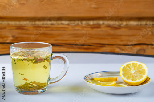 Lemgrass tea in a cup next to a lemon and sweets on a napkin on the table.