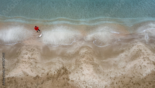 Aerial drone view of dog and woman playing at empty sandy beach with golden sand