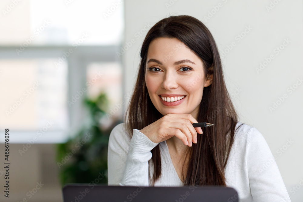 Portrait of a brunette woman working with a laptop in the office. The woman looks at the camera and smiles. Portrait of a brunette woman working with a laptop in the office. The woman looks at the camera and smiles.