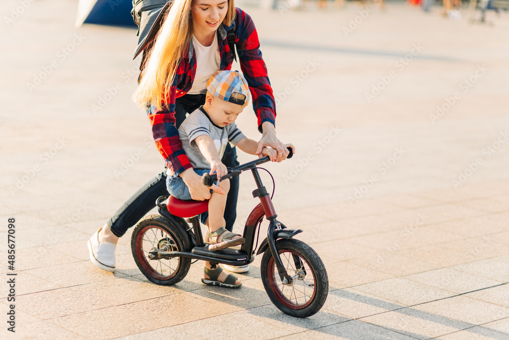 Fototapeta premium mother takes care of a child, training to ride a bicycle, running after her son in a public park