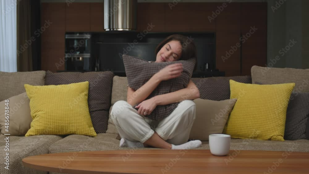 Calm young woman smiling hugs pillow sitting on cozy sofa in living room at home, resting, enjoying weekend Calm young woman smiling hugs pillow sitting on cozy sofa in living room at home, resting, enjoying weekend