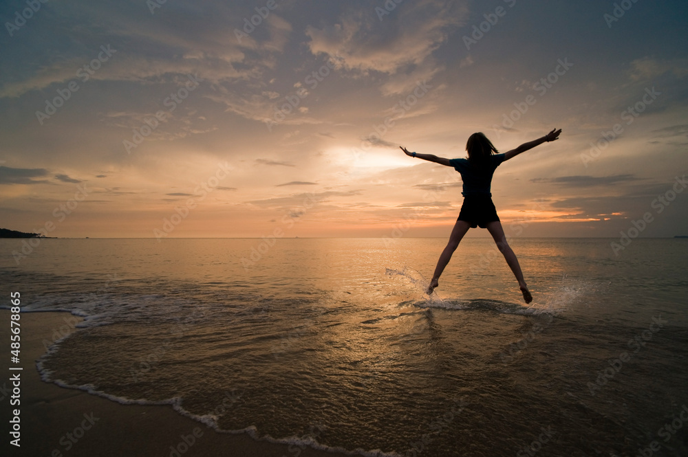 A young woman doing a star jump, enjoying her freedom on the beach at sunset., Thai Islands at Koh Samui, Thailand, Southeast Asia