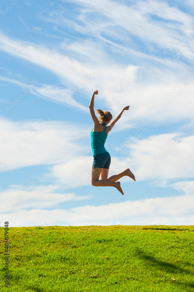 Happy woman jumping for joy, celebrating winning and enjoying happiness of freedom and carefree lifestyle on green grass with blue sky, background with copy space Happy woman jumping for joy, celebrating winning and enjoying happiness of freedom and carefree lifestyle on green grass with blue sky, background with copy space