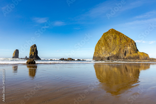 Haystack Rock in Cannon Beach, Oregon, with rocky coastline on a clear, blue sky afternoon.