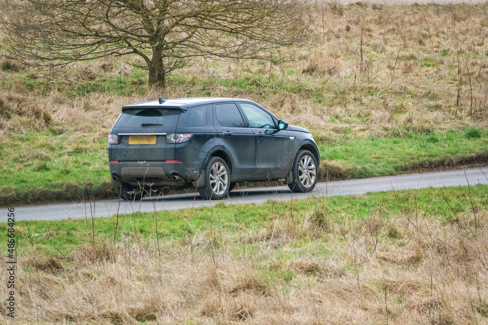 a black land rover discovery sport driving along a country road