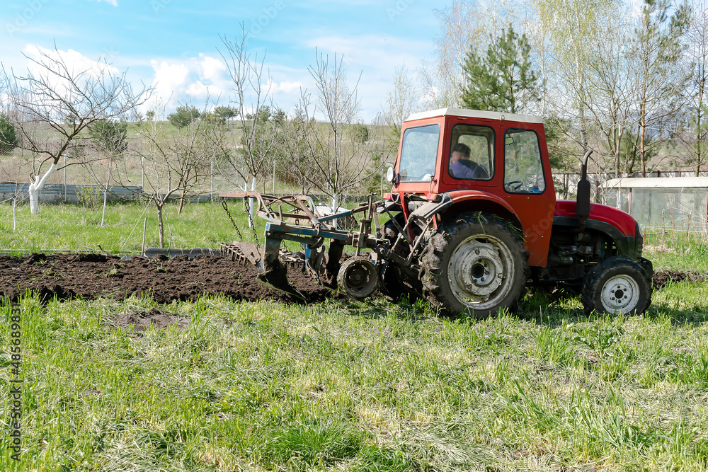 Modern red tractor machinery plowing agricultural field meadow at farm at spring autumn. Farmer cultivating and make soil tillage before seeding plants and crops, nature countryside rural scene Modern red tractor machinery plowing agricultural field meadow at farm at spring autumn. Farmer cultivating and make soil tillage before seeding plants and crops, nature countryside rural scene