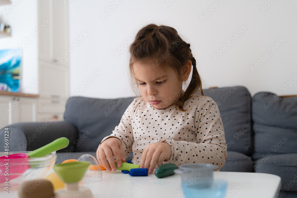 Close up view of the little kid girl sitting at the table and toying with colored figures Close up view of the little kid girl sitting at the table and toying with colored figures