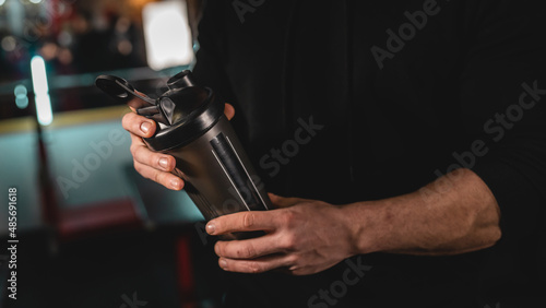 Close up on midsection of unknown caucasian man holding dark supplement shaker