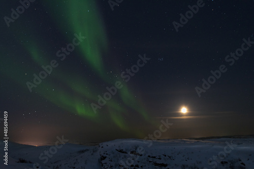 In winter, the moon and the aurora borealis are in the sky.