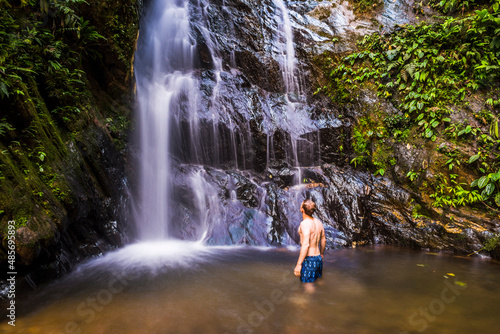 Fototapeta Naklejka Na Ścianę i Meble -  Tourist under Cucharillos Waterfall in the Mashpi Cloud Forest area of the Choco Rainforest, Pichincha Province, Ecuador, South America