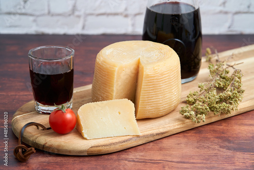 talian hard cheese such as pecorino or caprino, wine in carafe and a bunch of oregano with sliced cheese on a wooden board. Traditional Italian wine glass and tomato. 