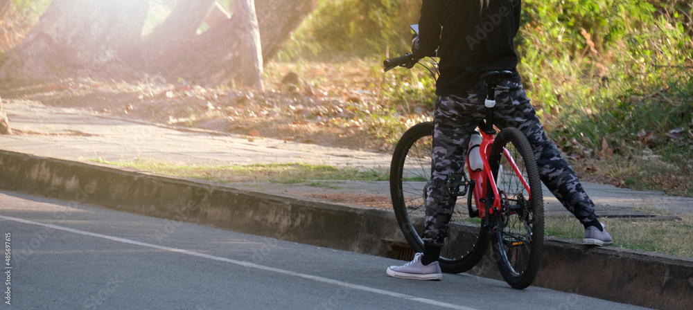 Fototapeta premium man in gym clothes sits on his red bicycle, stopping by the sidewalk.