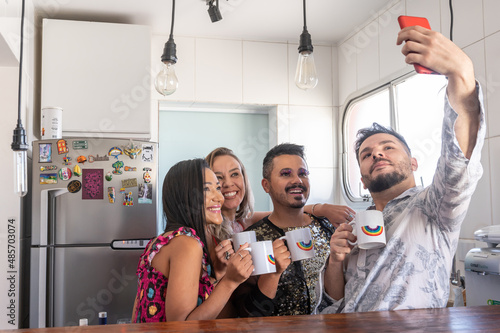 LGBT people holding ranbow mugs taking a selfie in the kitchen during the day, a fridge in the back, led lights on the top. photo