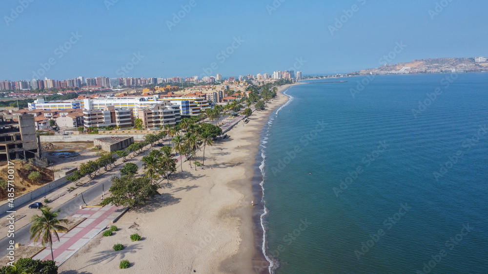 Aerial photos from a drone to a beach in Venezuela, where you can see beaches, residential areas, roads, trees, palms, sand, blue sky, residential hill, pools, roads, waves.