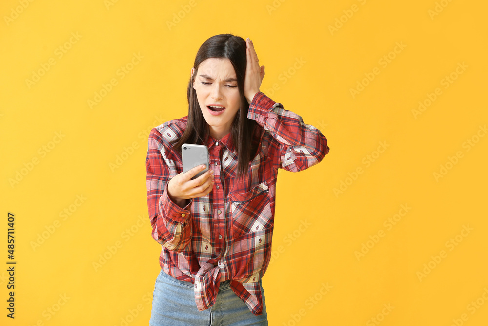 Fototapeta premium Troubled young woman with mobile phone on color background
